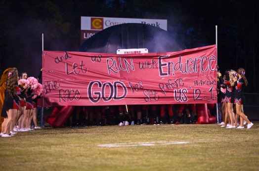 Cheerleaders holding banner with Bible verse