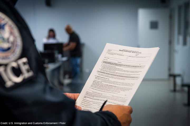 An ICE agent holding an Immigration Detainer form.