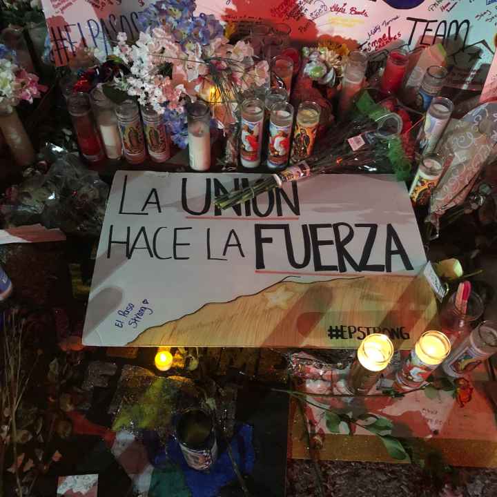 Photo: Handwritten signs, candles, and flowers adorn a section of a street. Pictured at center is a sign that says "La union hace la fuerza." 